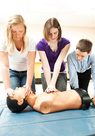 Two teenage girls and a boy practicing CPR life saving in school