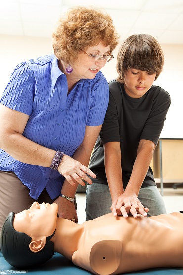 Teacher helping a teenage boy learn how to perform CPR.